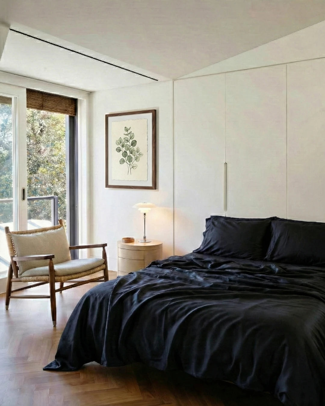 Modern bedroom with black bedding, white walls, and a chair by a window.