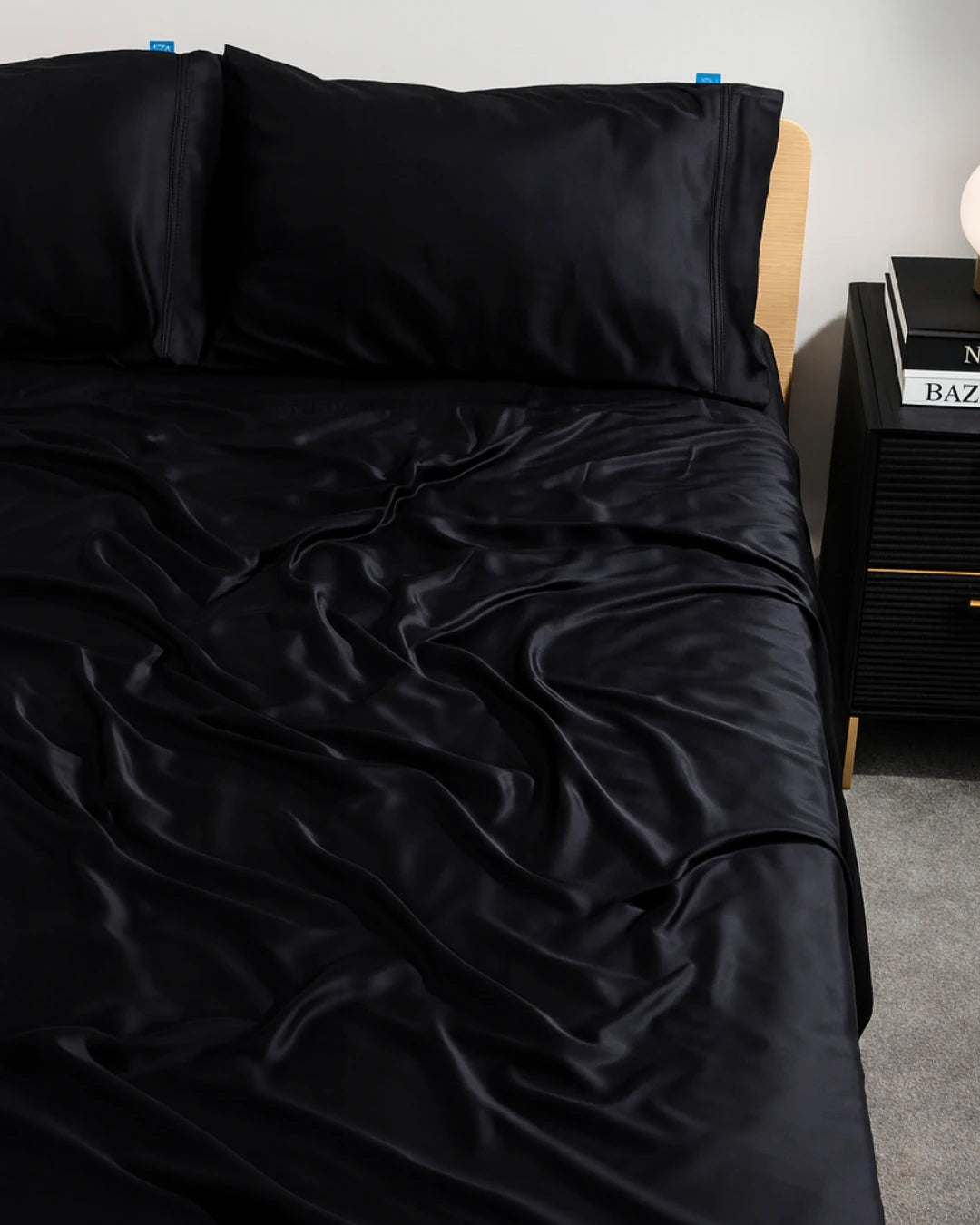 Black satin sheet set on a bed with a nightstand in the background.