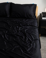 Black satin sheet set on a bed with a nightstand in the background.