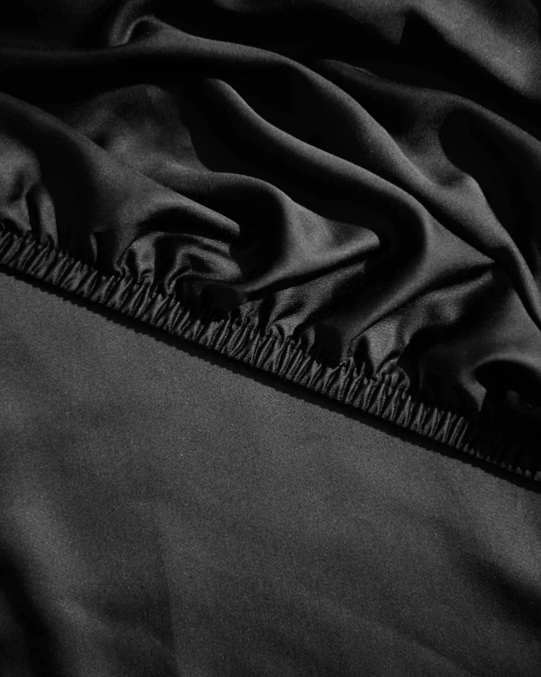 Black fitted sheet on a bed with a close-up view of the fabric texture.