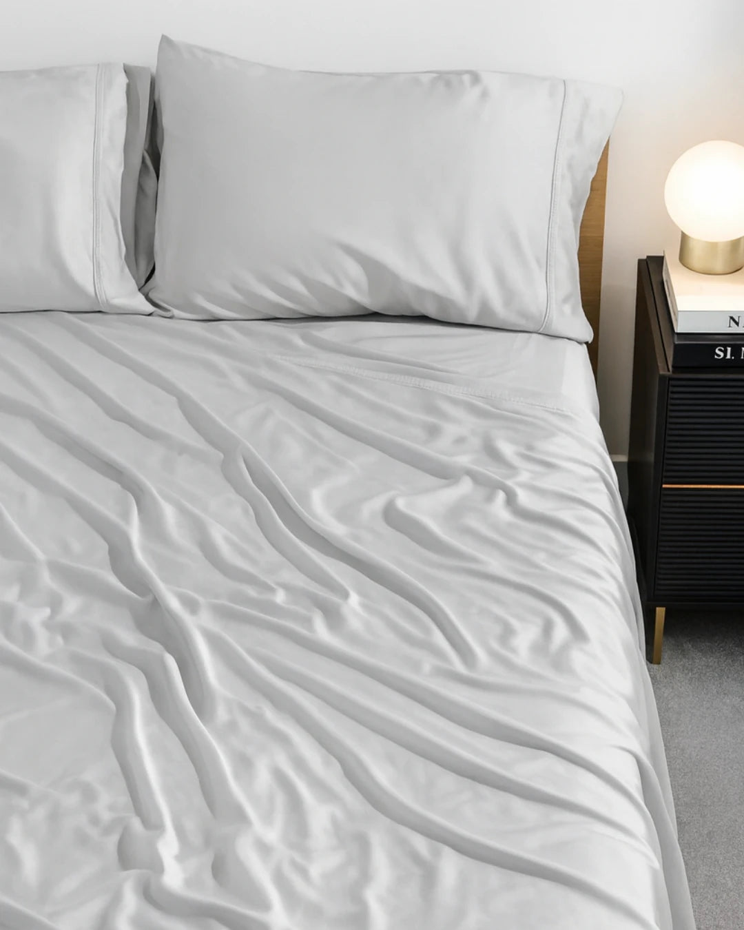 Gray bedding set on a bed with a nightstand and lamp in the background.