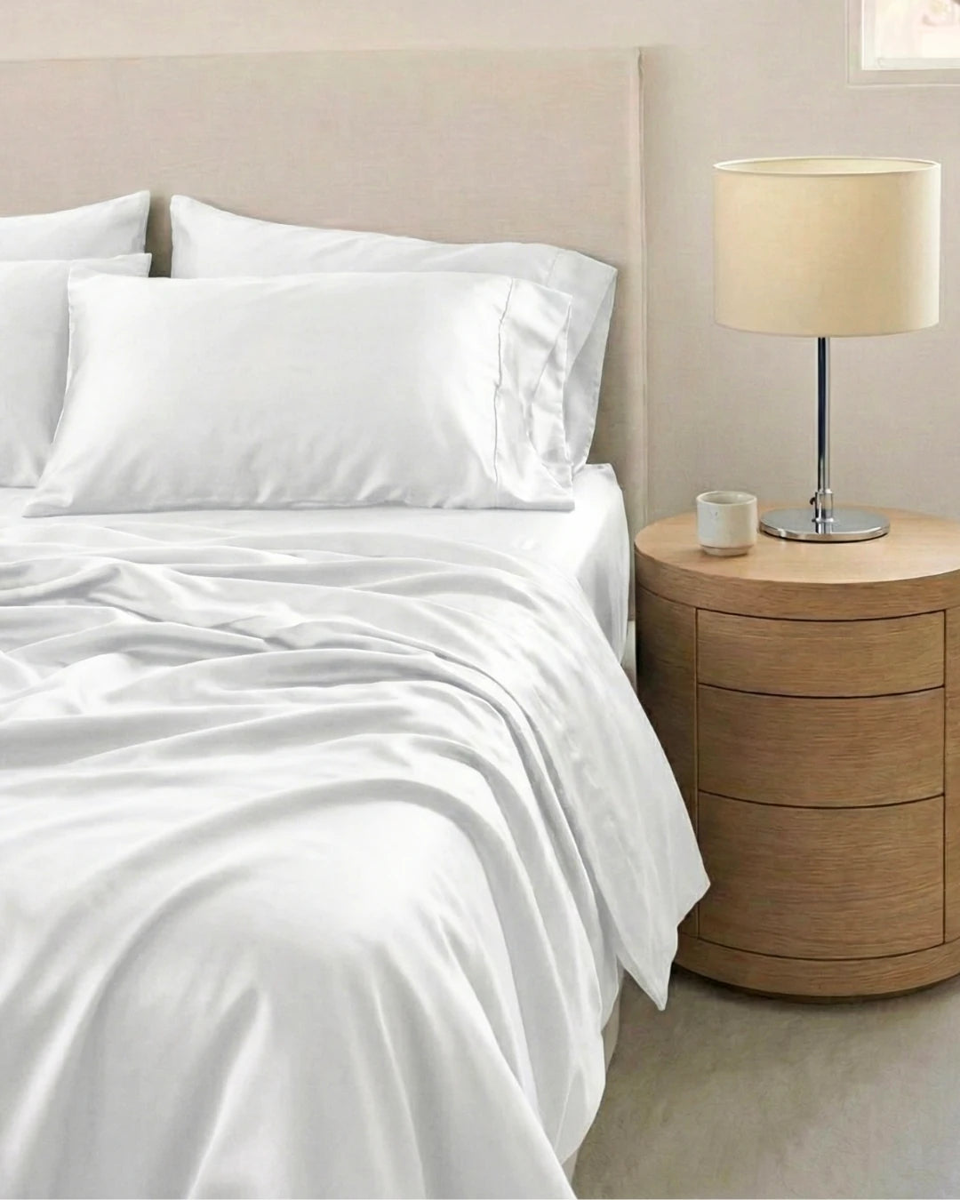 White bedding set on a bed with a wooden nightstand and lamp.
