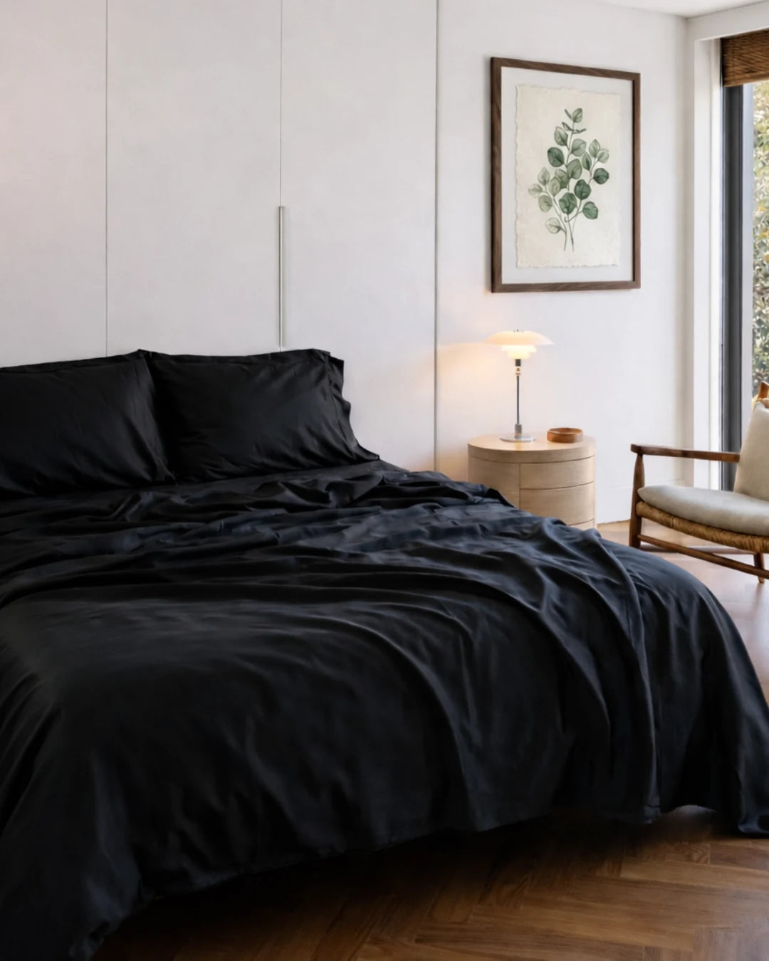 Bedroom with black bedding and a plant-framed picture on the wall.