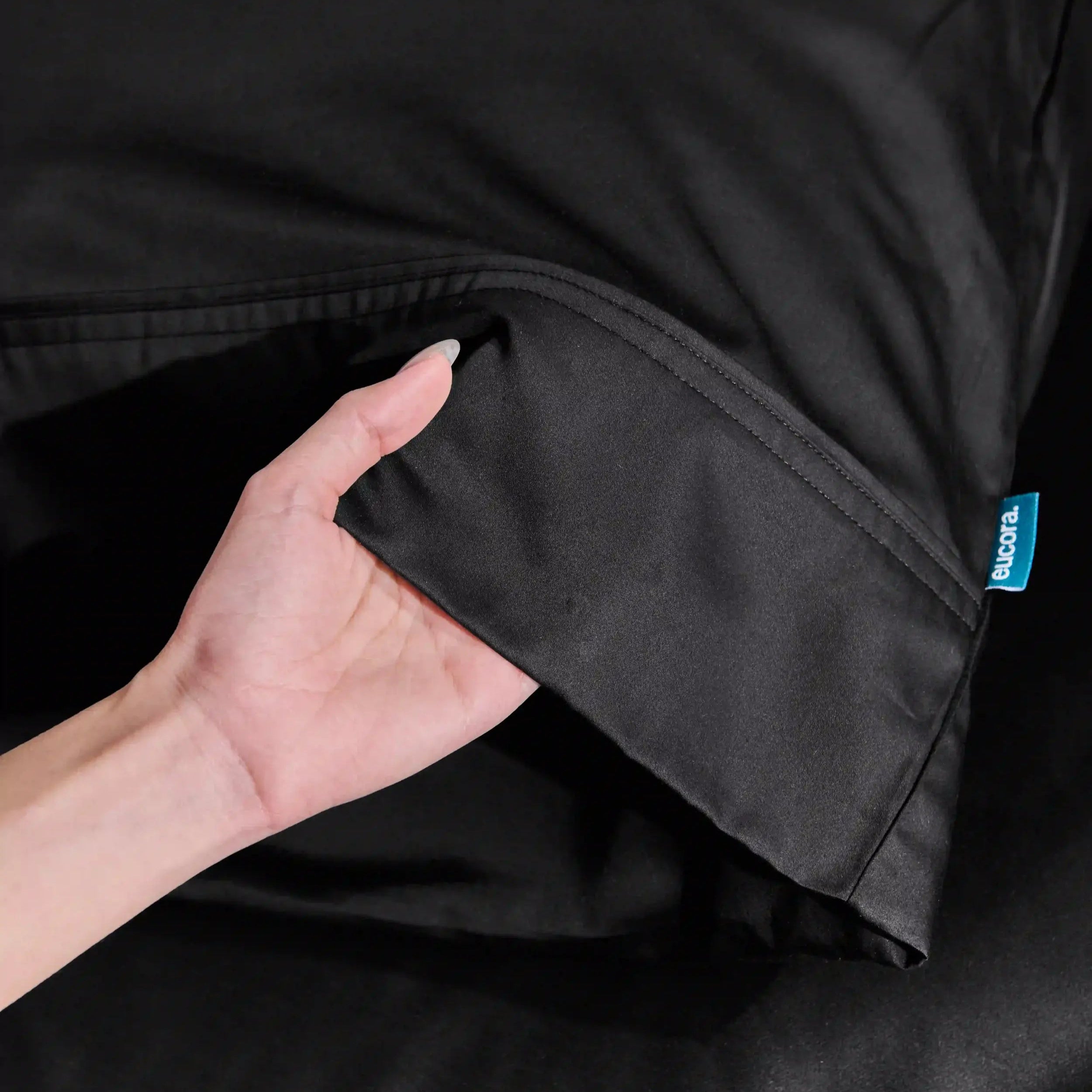 Close-up of a black jacket with a brand tag, held by a hand.