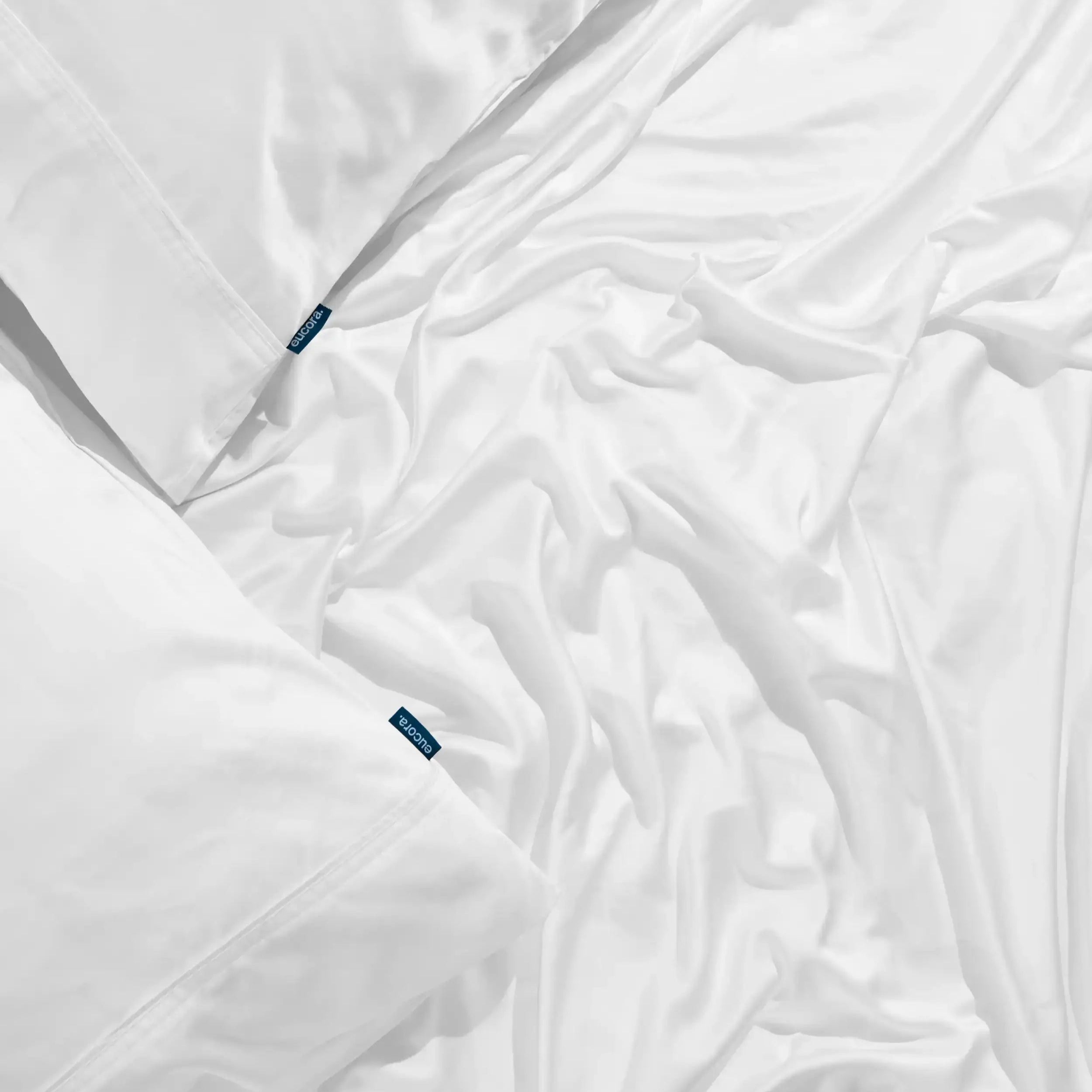 White bamboo bed sheets and pillows on a bed with visible Eucora Brand.